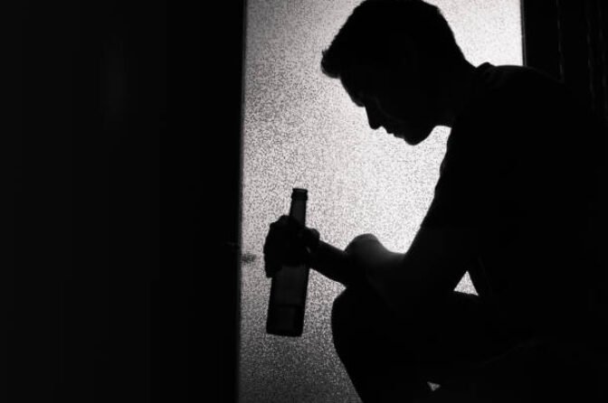 Man sitting at home and holding bottle of beer. Alcohol abuse concept.